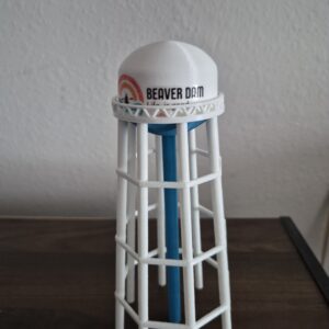 3D printed miniature replica of the Beaver Dam, Wisconsin water tower featuring the “Beaver Dam – Life is Good” logo with white tank, blue pedestal, and elevated white support legs.