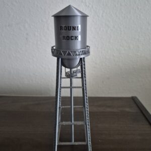 replica of the historic Round Rock, Texas downtown water tower with silver finish, steel-style support structure, and "ROUND ROCK" lettering.