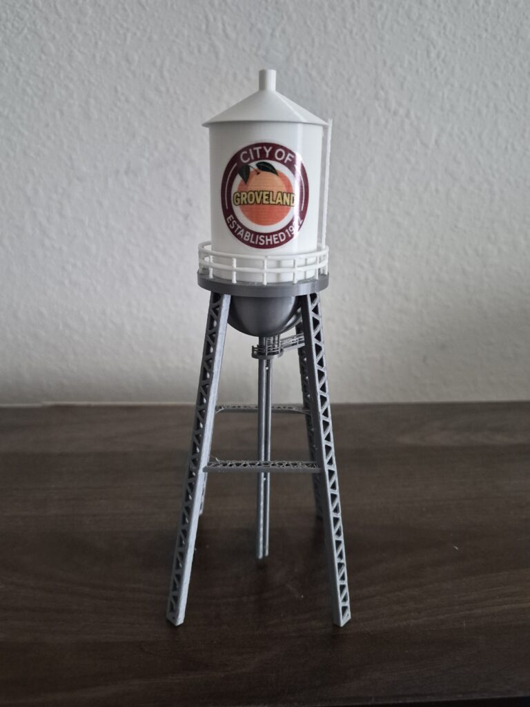 replica of the historic Groveland, Florida water tower with white cylindrical tank, orange city graphic, railing, and silver-gray support structure.