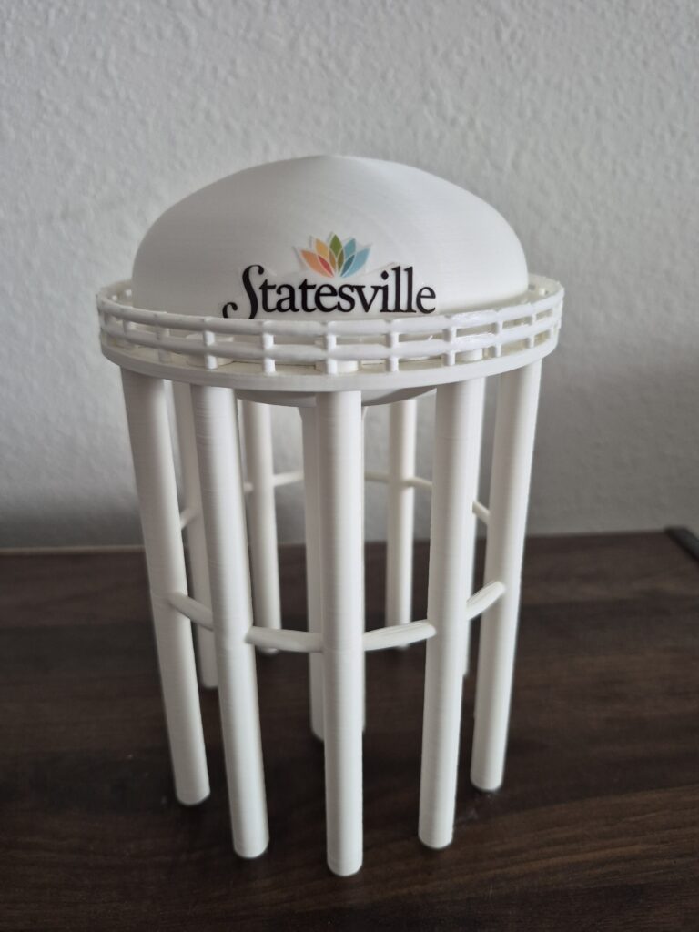 Statesville, North Carolina water tower replica featuring a rounded tank, colorful Statesville logo, circular railing, and multiple support columns.